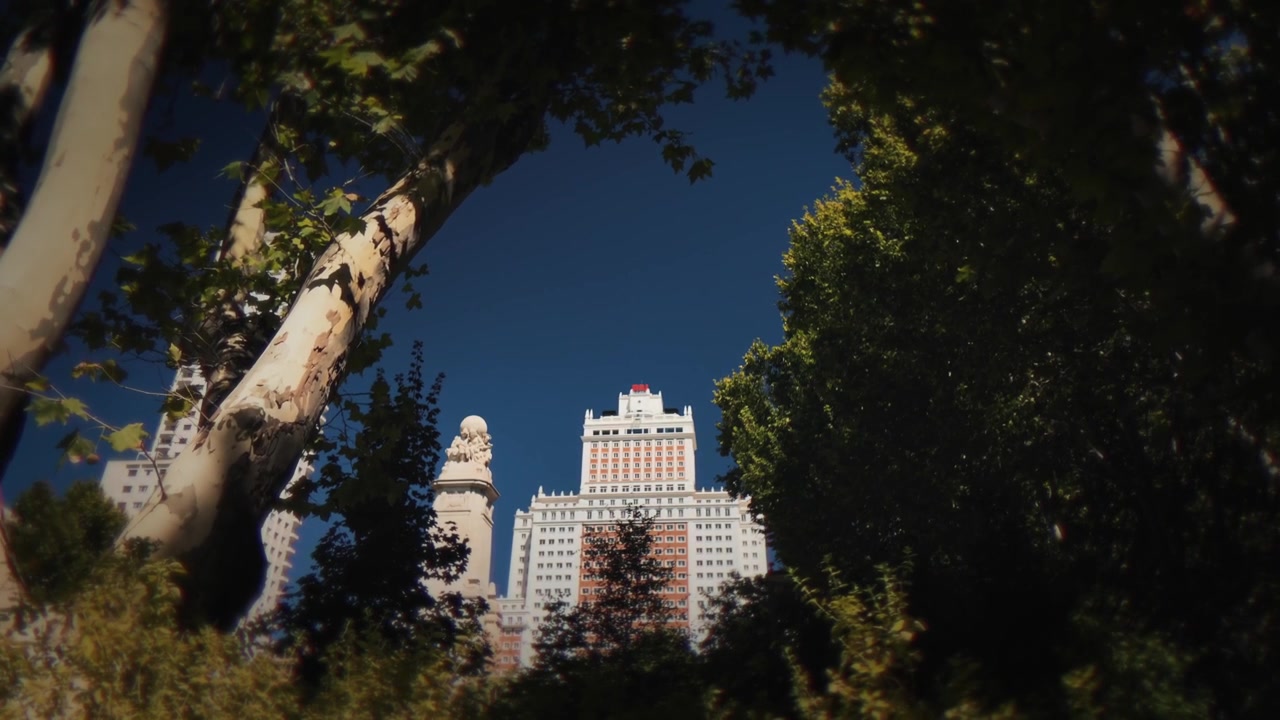 Vista lussureggiante degli edifici simbolo di Madrid che si ergono sopra gli alberi vicino al Monumento a Cervantes in Plaza de España