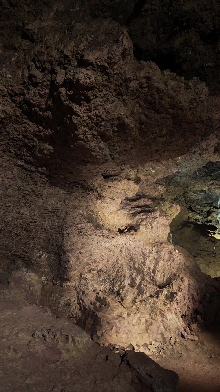 Rough rock walls of a Clearwell Caves chamber are picked out by spotlights, revealing textures and a rubble-strewn floor. vertical video