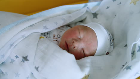 Sleeping tiny newborn baby in cap and blankets. Child opens mouth in his sleep. Close up.