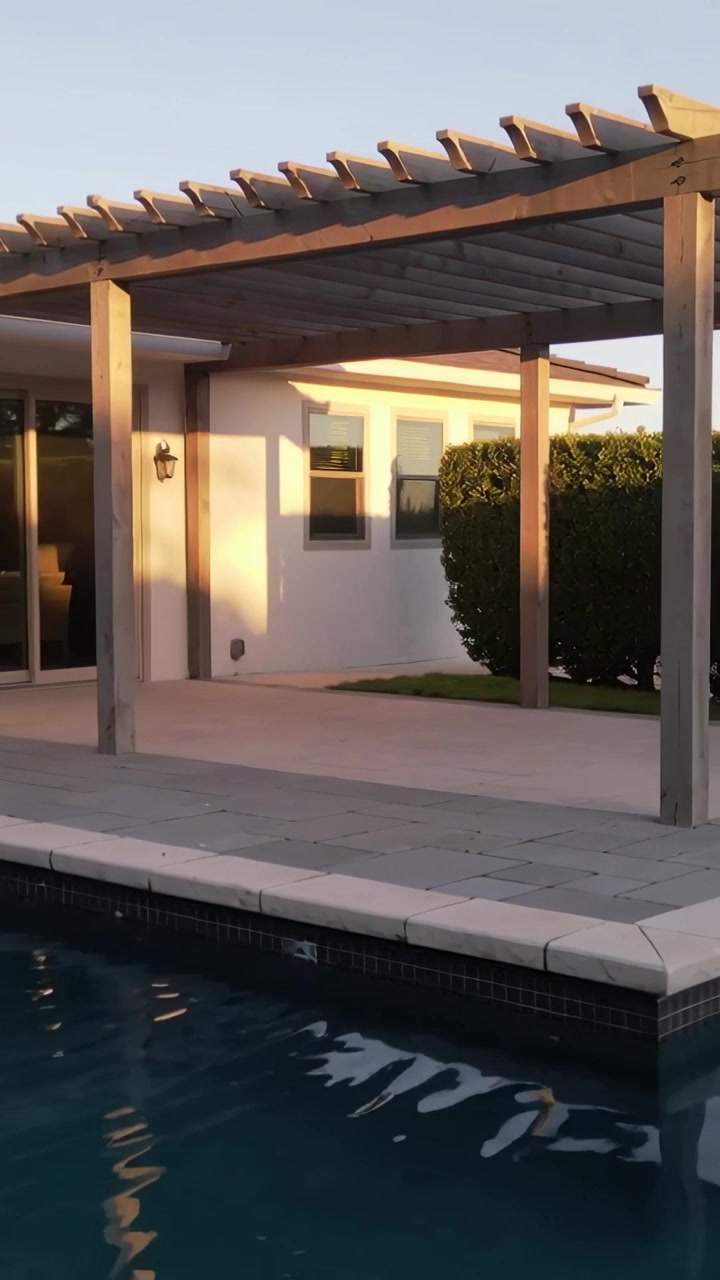 Vertikales Video: Schwenkende Kamera enthüllt gefliesten Pool und Pergola auf einer Gartenterrasse, zeigt goldenes Licht.