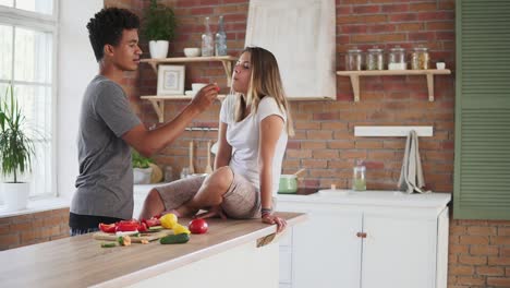 Toma-En-Cámara-Lenta-De-Una-Atractiva-Pareja-Multiétnica-Charlando-En-La-Cocina-Temprano-En-La-Mañana.-Hombre-Guapo-Alimentando-A-Su-Esposa