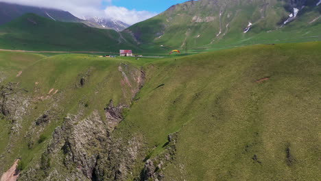 wide rotating drone shot of paraglider flying near a cliff in the caucasus mountains in gudauri georgia