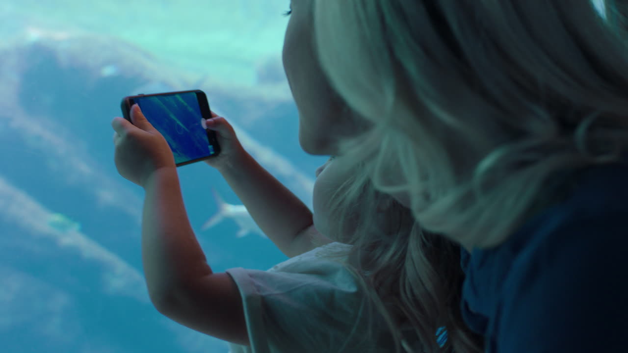 niña tomando fotos de peces en el acuario usando un teléfono inteligente madre e hija fotografiando la vida marina nadando en el tanque con la cámara del teléfono móvil divirtiéndose en el oceanario compartiendo en las redes sociales