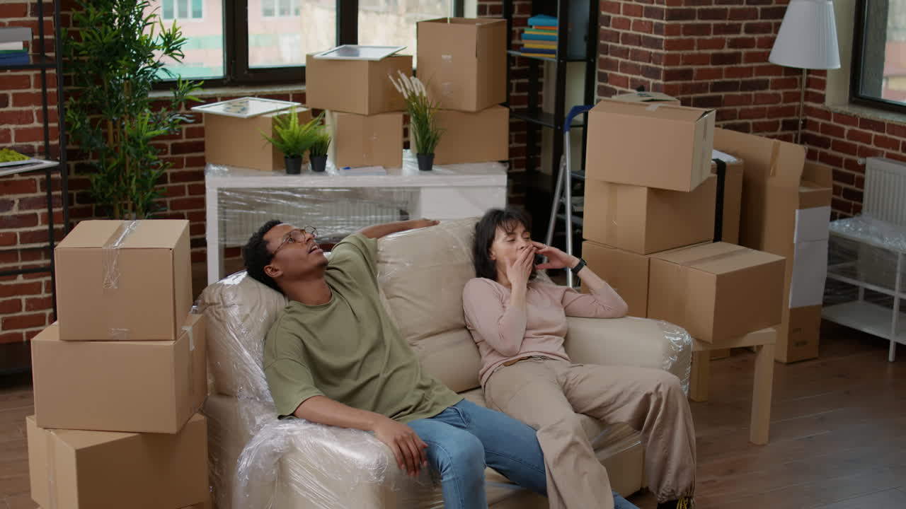 Tired husband and wife relaxing on couch after unpacking furniture