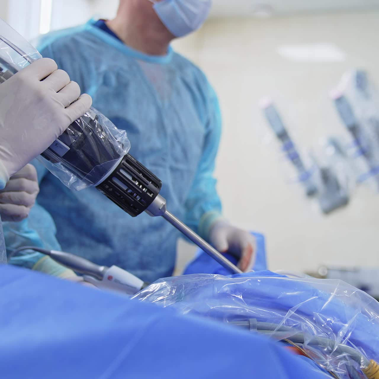 Advanced robotic equipment in the hands of a surgeon applied to a patient. Doctor uses device moving it quickly. Da Vinci robot at backdrop in blur
