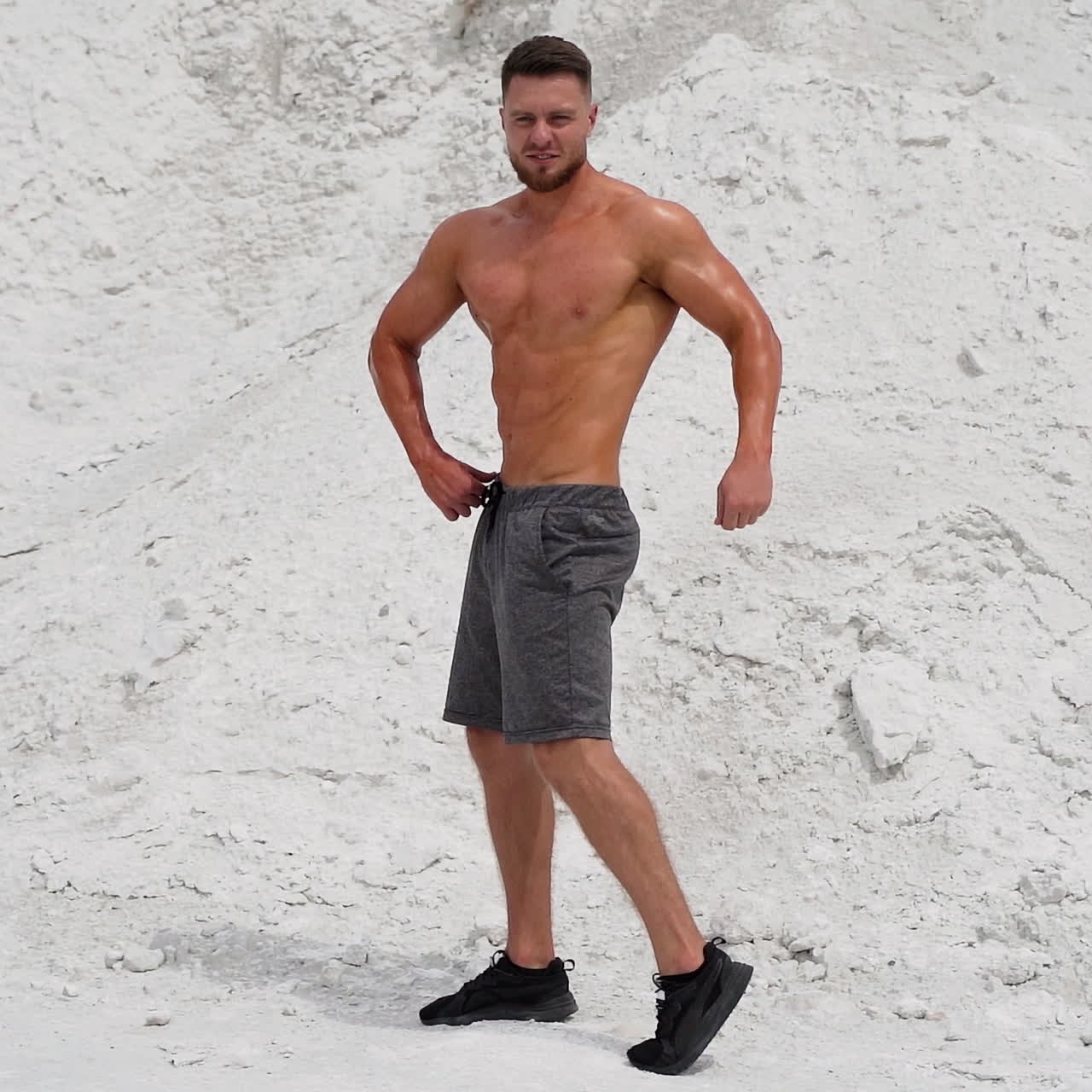 Full-length portrait of a bodybuilder outdoors. Young man with muscular body posing to camera on white mountain background.