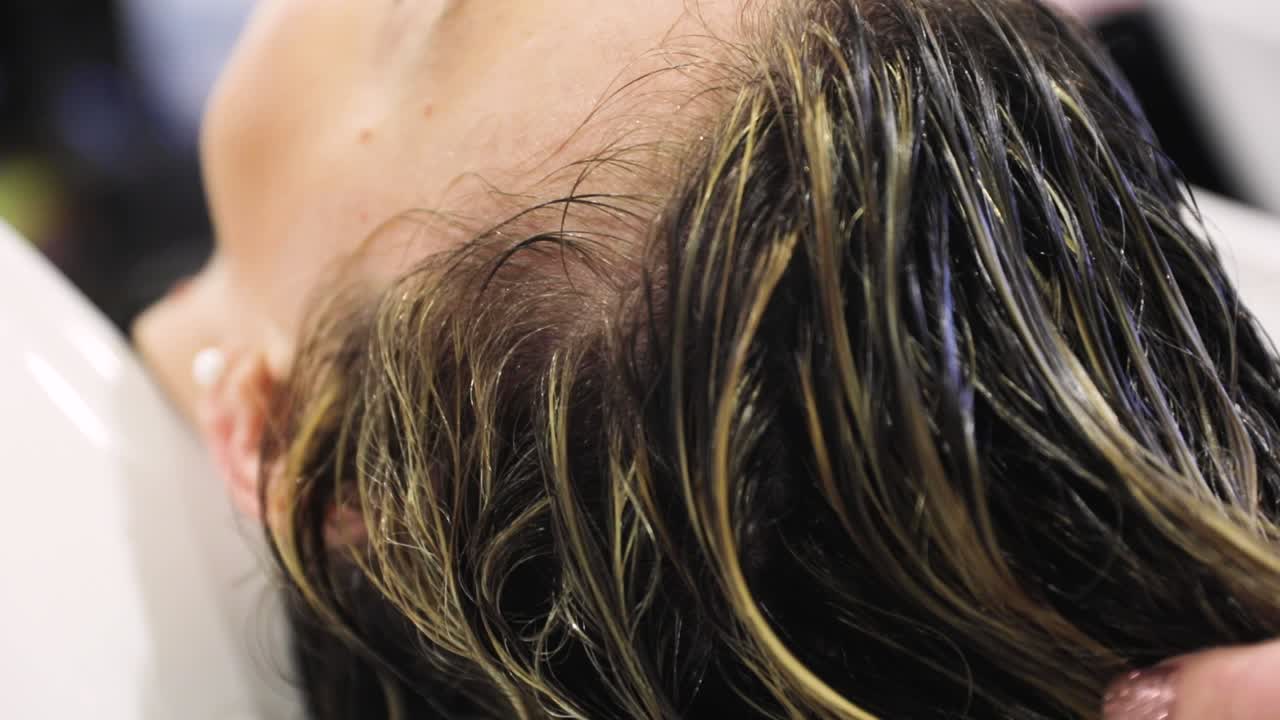 Close-up caring hands female hairdresser washing hair to woman