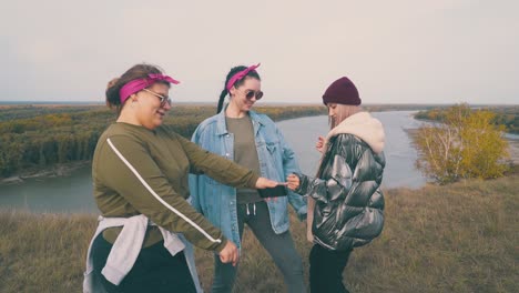 girls choose music with phone on river edge at sunset