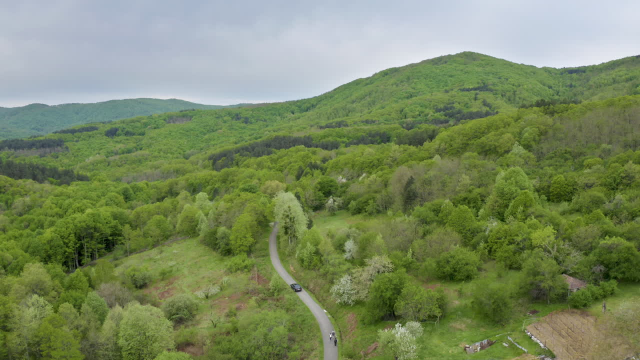 Approaching drone shot on a car going up a winding road, passing by some villagers from a nearby farm as it goes up to the Golyamo Gradishte Peak in Strandzha Mountain in Bulgaria.