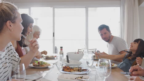 multi generation family sitting around table at home eating meal together