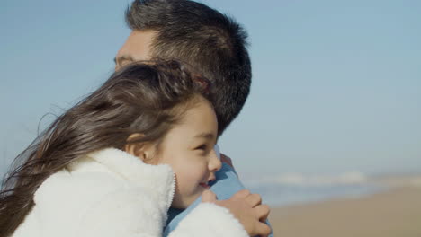 close up shot of happy japanese dad embracing his cute little daughter at the beach