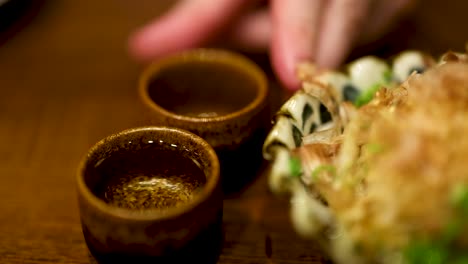 hand reaching for sake cup beside food