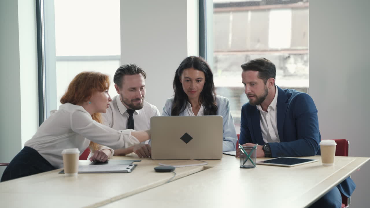 A young working team composed of two women and two men consulting the laptop together in a work meeting