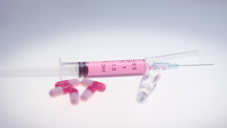 syringe with pink liquid. pharmaceutical pills and medical glass ampule