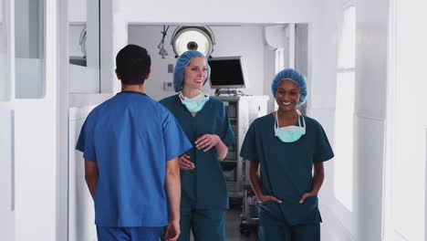 two female surgeons wearing scrubs having meeting as they walk along busy hospital corridor together