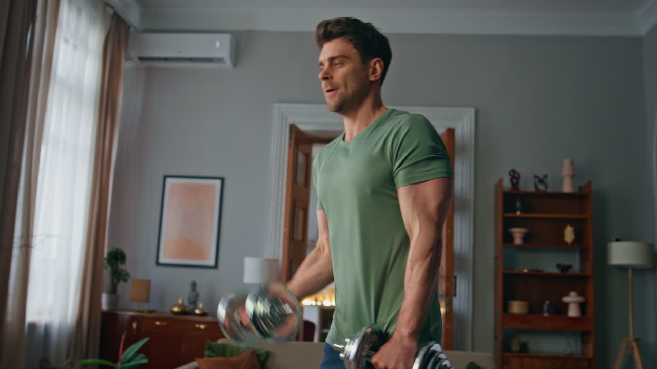 Tensed athlete exercising dumbbells in apartment close up. Man lifting equipment