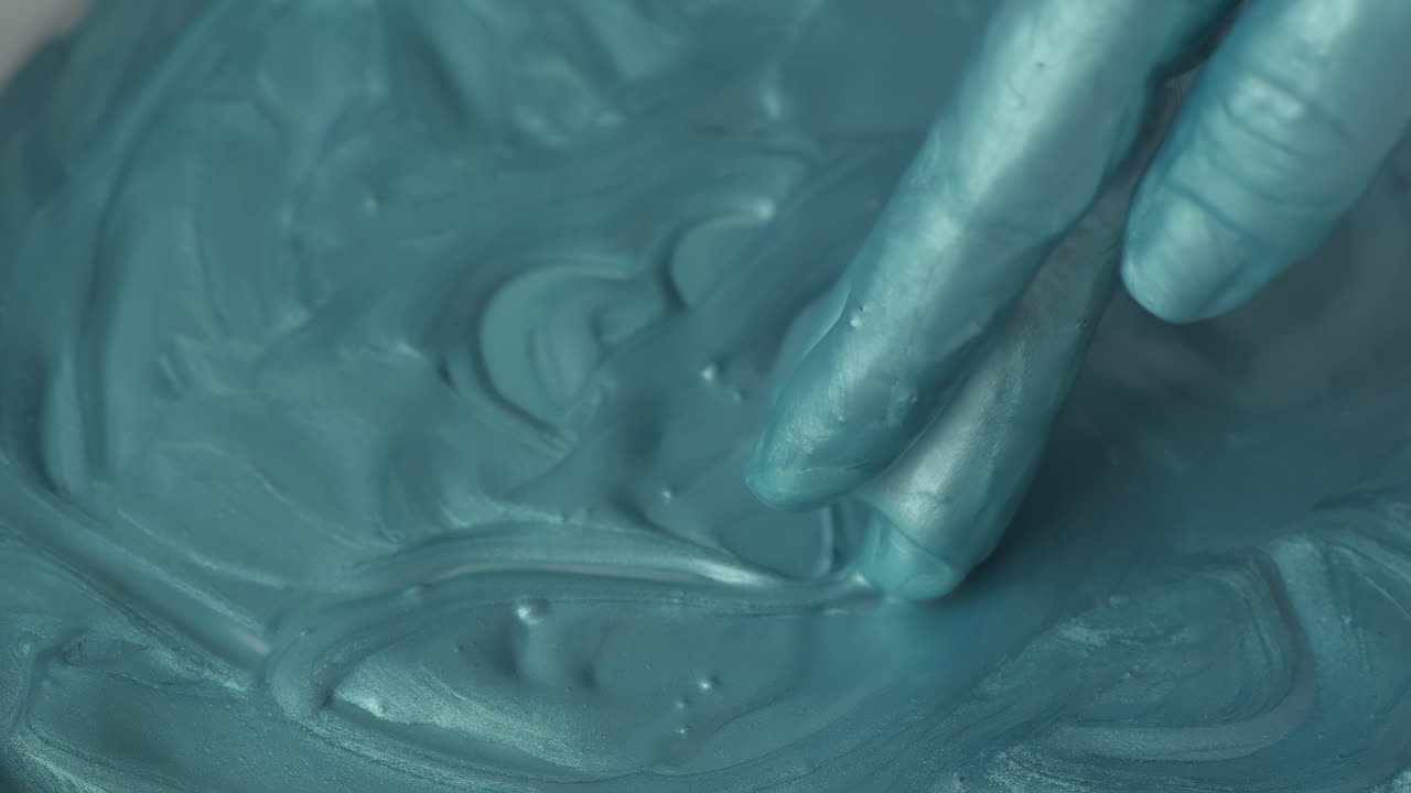 A close-up of a hand mixing vibrant blue paint with fluid textures on a canvas in a bright, inspiring studio environment. The colors blend beautifully