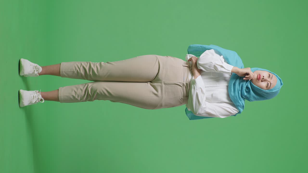 아시아 무슬림 여성이 생각하고 주위를 둘러보며 초록색 스크린 배경 스튜디오에 서있는 동안 지표손가락을 들어 올립니다.