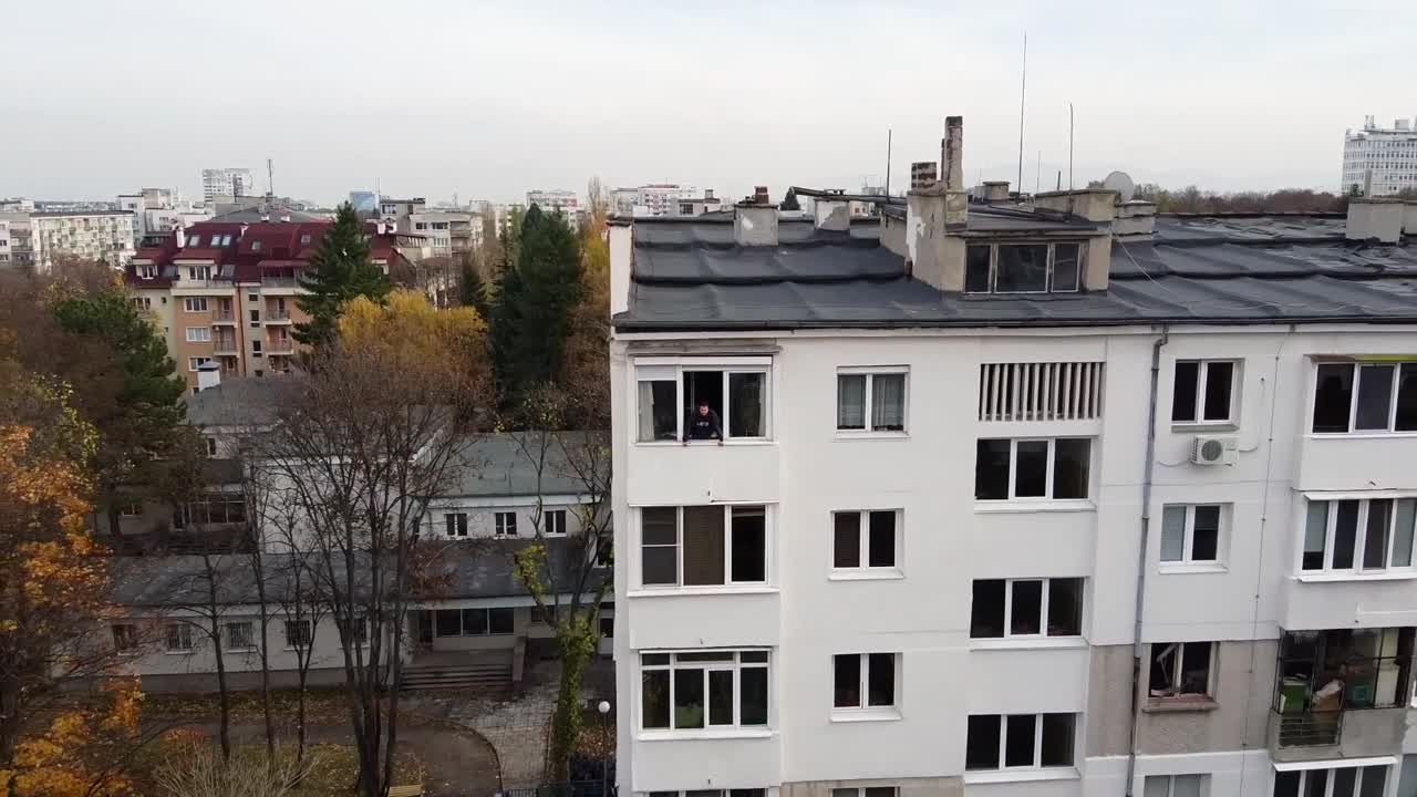 Person looking out from an apartment window in an urban setting