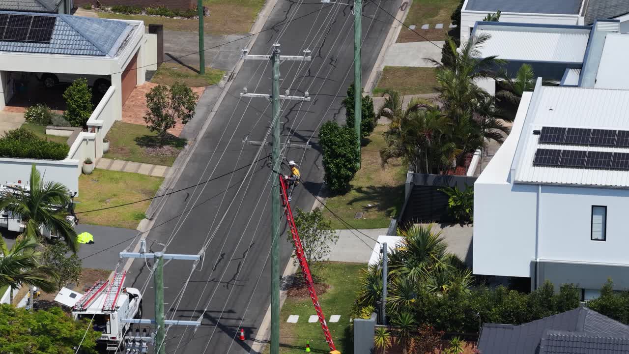 Aerial view of utility worker in safety gear servicing power pole on sunny suburban street