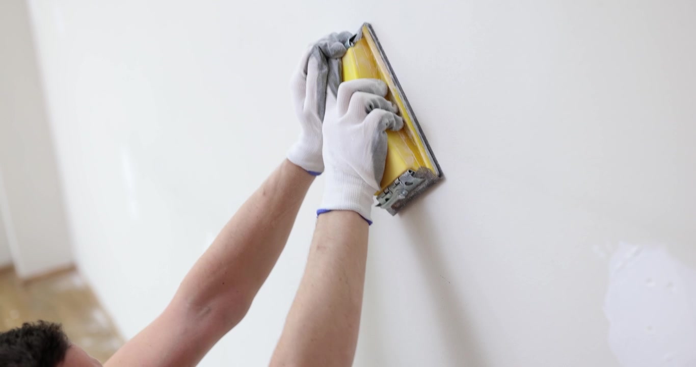 Construction worker polishes surface of wall using spatula