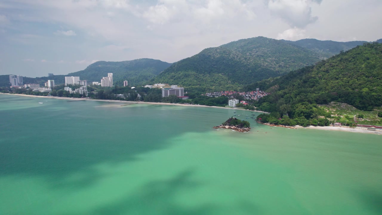 Amplia vista aérea de la isla de Penang, donde el mar turquesa se encuentra con montañas cubiertas de bosque y una costa desarrollada, capturando la belleza tropical de Malasia desde arriba
