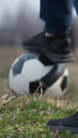 blurred close-up of a football being passed between two people on a grassy field, with one person trapping the ball under their right foot, the background features a blurred grassy field