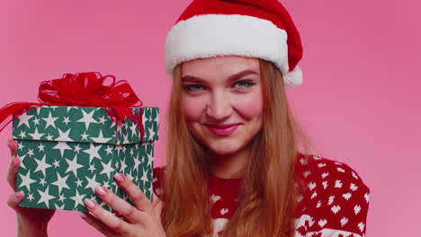 Cheerful-lovely-girl-in-sweater-Santa-hat-presenting-one-Christmas-box,-excited-by-holiday-gift