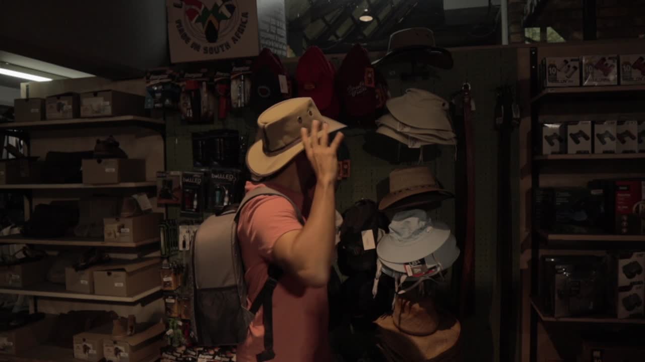 macho probándose sombreros dentro de una tienda de souvenirs en el parque nacional kruger sudáfrica