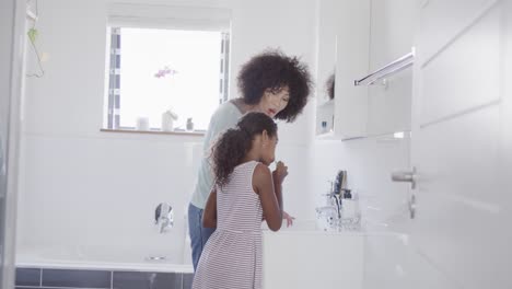 happy african american mother and daughter brushing teeth in bathroom, slow motion