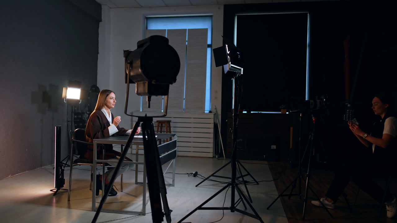Modern photo studio with equipment for filming a video. Female blogger taking video for her blog. Caucasian girl sitting backstage uses her phone for footage.