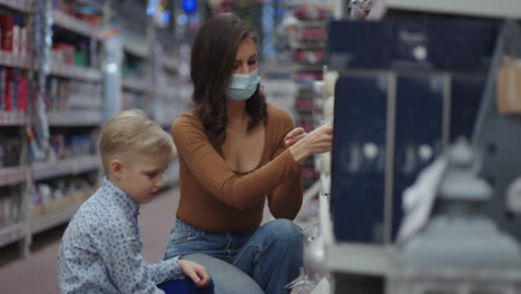una madre enmascarada elige juguetes navideños con su hijo antes de navidad