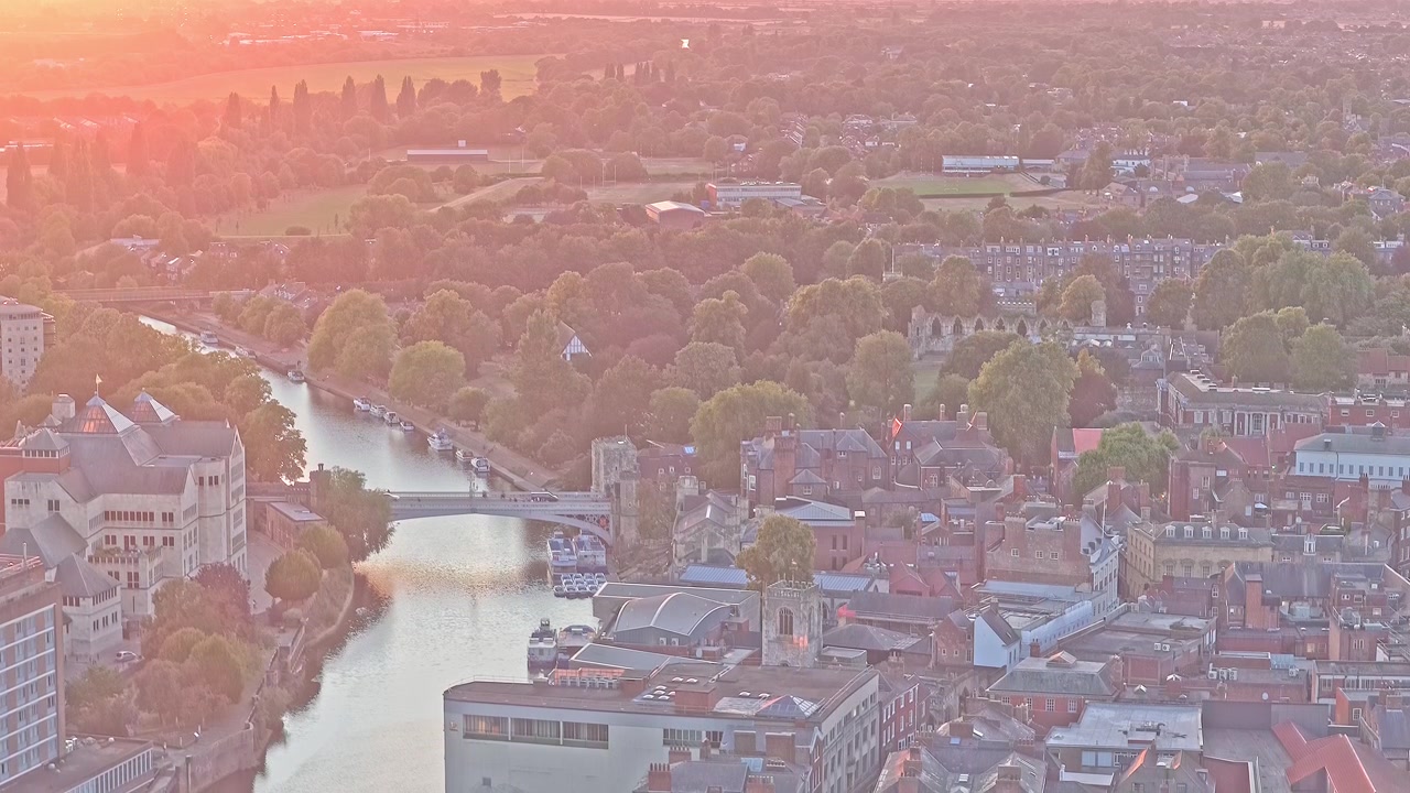 Il Ponte Lendal attraversa il fiume Ouse accanto alla Lendal Tower nel centro di York, con edifici lungo il fiume, parchi verdi e architettura storica che si estendono lungo il corso d'acqua, discesa del drone.