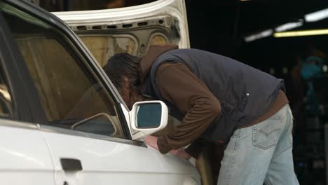 El-Mecánico-Se-Acerca-Al-Viejo-Auto-Blanco,-Levanta-El-Capó-Y-Mira-Dentro