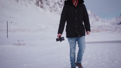 man holding digital video camera walks in snow, travel in nature with modern technology