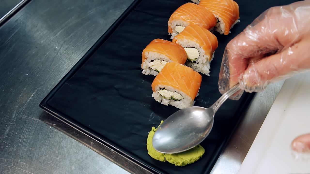 Japanese sushi rolls on a black board. Serving food by the chef. Putting wasabi on the board