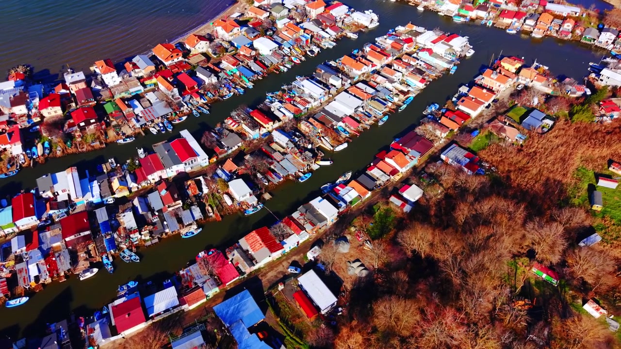 Flygfoto över färgglada tak längs en fiskekanal, Bulgarien. Drönarperspektiv av hus, förtöjda båtar och en smal vattenkanal