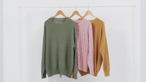 video of three multi coloured sweaters on hangers and copy space on white background