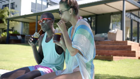 diverse couple enjoying drinks by pool, wearing summer clothes, at home