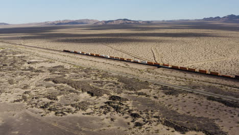 Tren-De-Carga-Extremadamente-Largo-Con-Muchos-Vagones-De-Tren-Acelera-Por-Una-Vía-De-Tren-A-Través-De-Un-Paisaje-Desértico