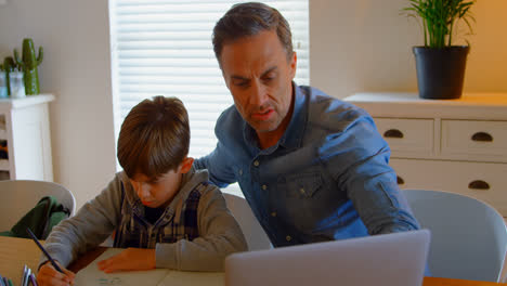 Front-view-of-young-Caucasian-father-helping-son-with-homework-at-table-in-a-comfortable-home-4k