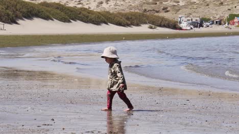 2 years old little girl with bucket hat walking alone in the beach on a sunny summer day