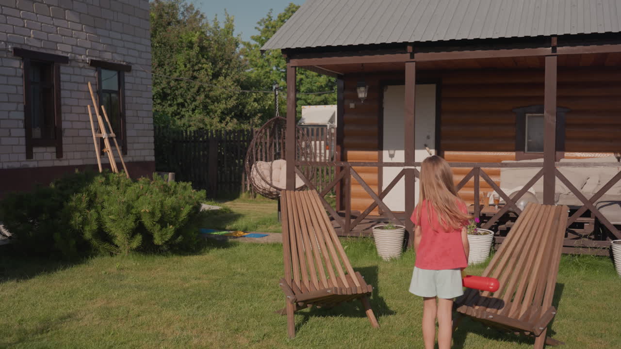 Child Near Cottage, Girl Playing Outside On Lawn, Young Girl Standing By Cottage Doorway Engaging Imagination, Child With Toy On Sunlit Lawn By Wooden Furniture Embracing Curiosity