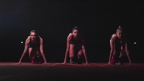 Three-girls-in-black-clothes-are-in-the-starting-pads-to-start-the-race-in-the-competition-in-the-light-of-lanterns.