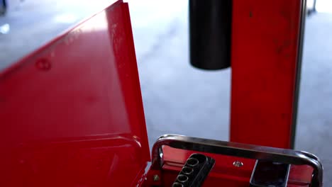 Mechanics-bright-red-toolbox-full-of-tools,-with-cell-phone-android-sitting-on-ledge,-with-sockets-and-equipment-in-focus-as-camera-pans-up-to-reveal-garage-shop-with-car-on-lift