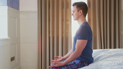 Man-Sitting-On-Edge-Of-Bed-At-Home-Meditating-During-Lockdown-For-Covid-19