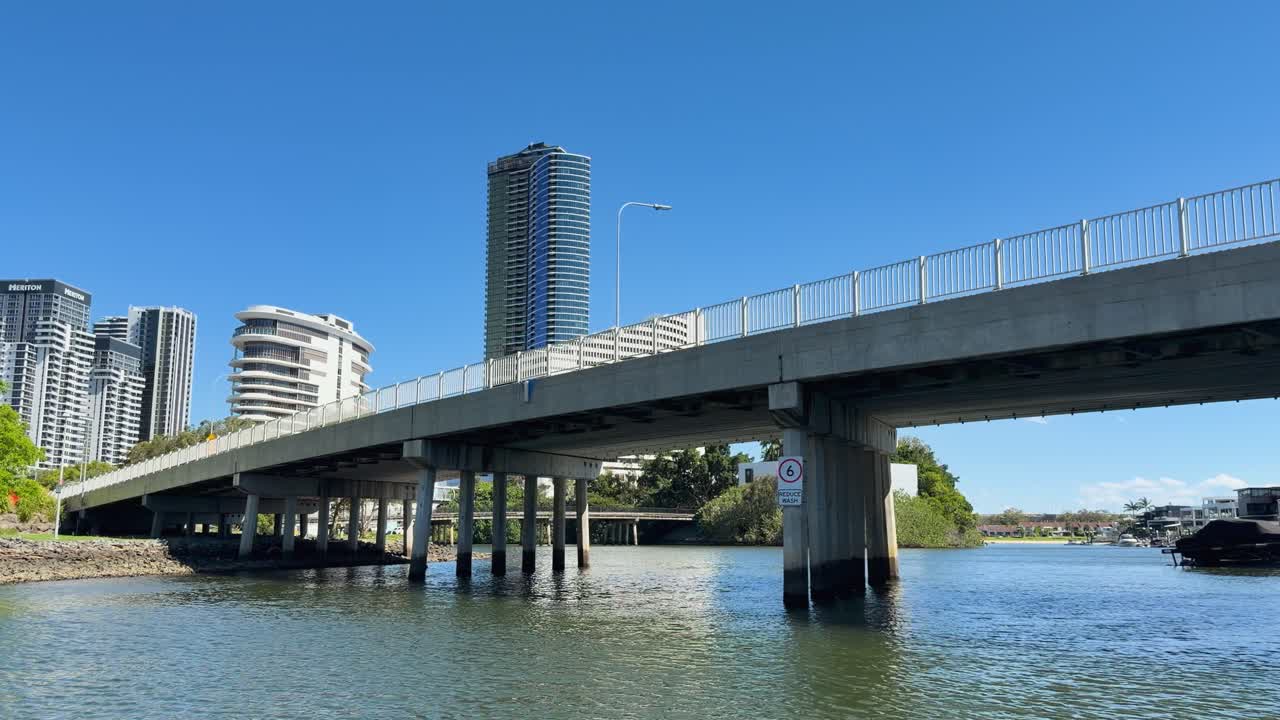 Smooth camera movement under concrete bridge, revealing riverside skyscrapers, houses, and clear blue sky