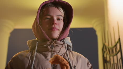 elegant girl standing outdoors holding pastry in hand, dressed warmly under glowing night clock, calm expression, cool weather ambiance, and illuminated urban backdrop