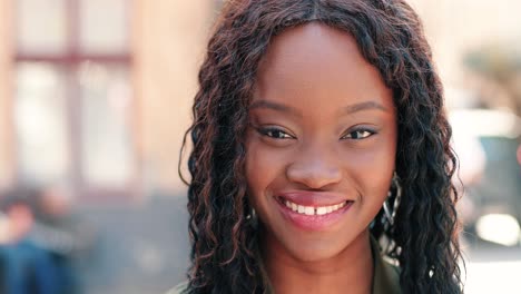 close-up view of african american woman with curly hair looking at camera and smiling in the street