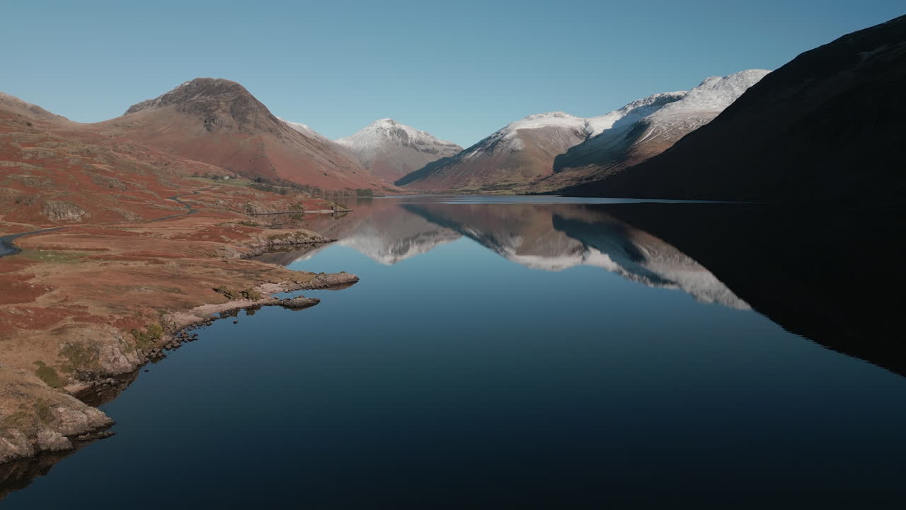 Stiger op over en rolig sø med sneklædte bjerge reflekteret i vandet ved Wastwater, Lake District, Storbritannien.